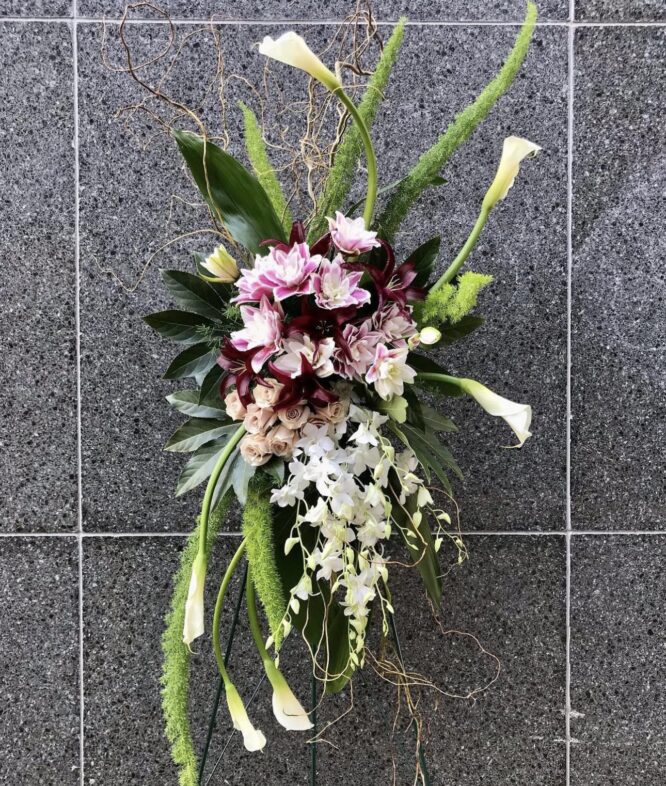 Stylish standing spray featuring white, burgundy, and green flowers, designed for funerals and memorial services."