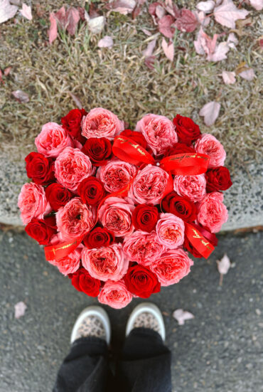 Heart-shaped box filled with vibrant garden hot pink and red roses, beautifully arranged for a romantic gift.