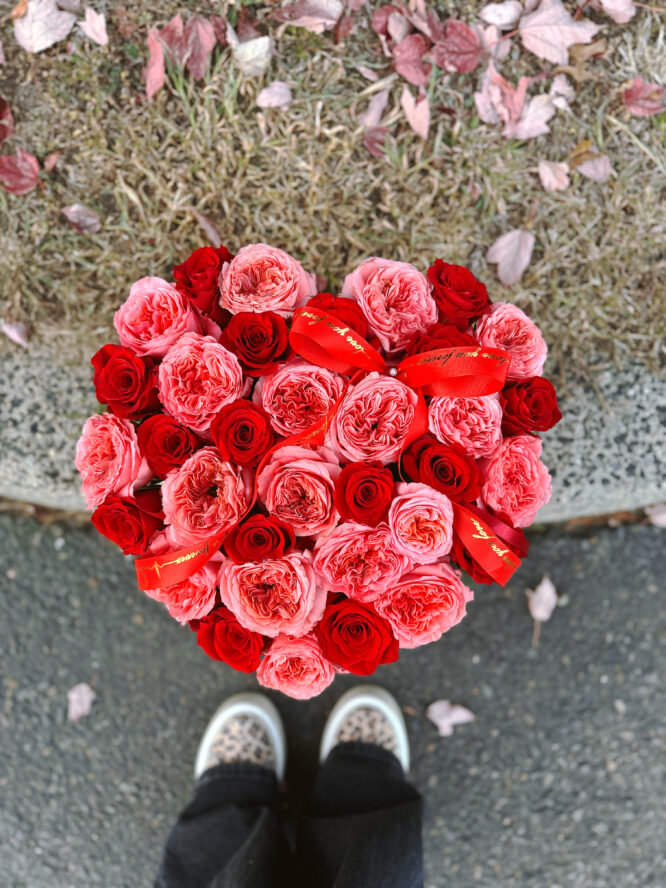 Heart-shaped box filled with vibrant garden hot pink and red roses, beautifully arranged for a romantic gift.