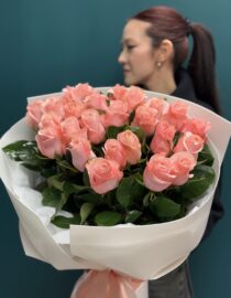 Elegant bouquet of 25 soft pink roses wrapped in white paper with a pastel satin ribbon." "Romantic floral arrangement of fresh pink roses with lush greenery." "A person holding a stunning bouquet of 25 soft pink roses in delicate wrapping."