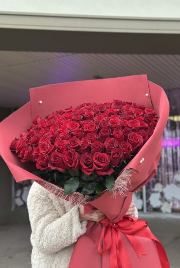 Extra-large bouquet of 101 premium red roses wrapped in elegant red paper with satin ribbons." "Luxurious arrangement of deep red roses, perfect for grand romantic gestures." "A person holding a stunning bouquet of 101 red roses in elegant wrapping."