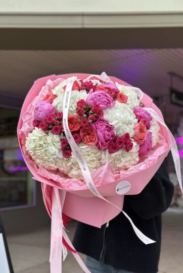 A large bouquet of white and bright pink flowers, including hydrangeas, peony-like roses, and spray roses."